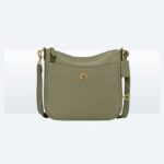 Olive green leather crossbody bag resting on an open suitcase in a sunlit hotel room.