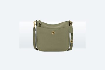 Olive green leather crossbody bag resting on an open suitcase in a sunlit hotel room.