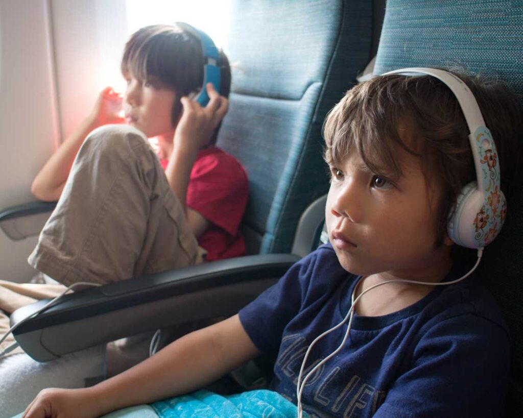 A toddler wearing comfortable blue headphones while looking out an airplane window.